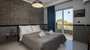 A modern hotel room with a large bed, a brick accent wall, a balcony with a view, and a mounted picture of a classic car. - Villa Lilienne - Tranquil Escape With Private Garden Balcony (Rhodes)