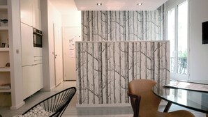 A modern kitchen with white cabinetry, a built-in oven, a dining area with a glass table, and a wall with a tree pattern.