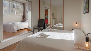 Ein Hotelzimmer mit einem großen Bett, einem Sessel, einem Schreibtisch und Blick auf die Stadt durch ein Fenster.