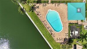 An aerial view of a property with a swimming pool, patio area, and a small building with a green roof.