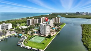 A coastal hotel with multiple high-rise buildings, a marina with boats, and a tennis court.