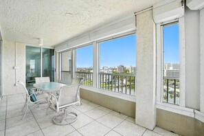 A balcony with a glass door leading to a room, a round table with chairs, and large windows offering a city view. - Vanderbilt Beach Views from 2 Lanais (Naples)