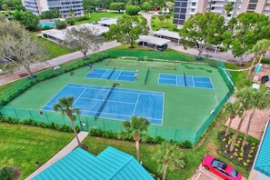 An aerial view of a tennis court complex with multiple courts, surrounded by greenery and residential buildings.