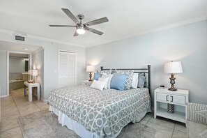 A bedroom with a bed, two bedside tables, a nightstand, a ceiling fan, and a door leading to a bathroom. - Vanderbilt Beach Views from 2 Lanais (Naples)