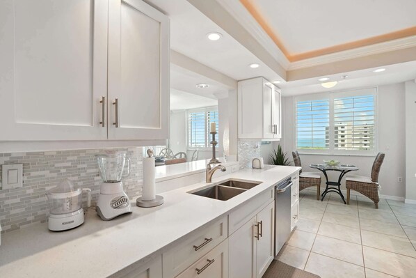 A modern kitchen with white cabinets, a built-in sink, a blender, and a dining area with wicker chairs.