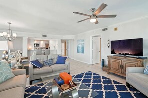 A modern living room with a grey sofa, blue and white patterned cushions, a coffee table with decorative items, a blue and white rug, a ceiling fan, and a flat-screen TV on a wooden cabinet. - Vanderbilt Beach Views from 2 Lanais (Naples)