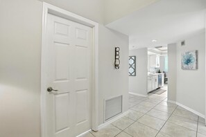 A hallway with a white door, a vent, and a kitchen area in the background.