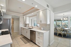 A modern kitchen with white cabinetry, a dishwasher, and a dining area with a round table and chairs.