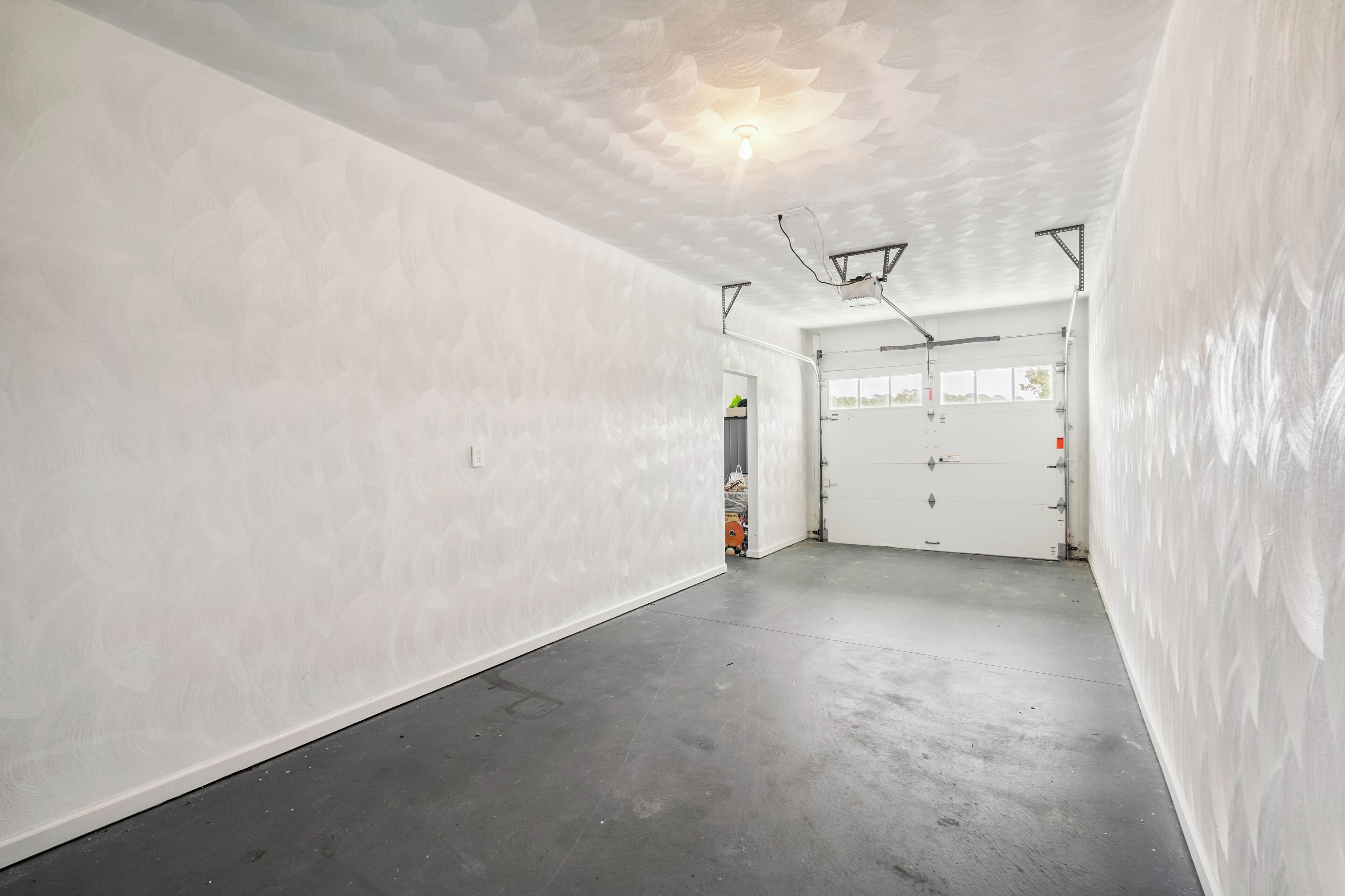A spacious, empty room with white walls and a concrete floor, featuring a ceiling light and a door with a window.