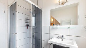 Een moderne badkamer met een douchecabine van glas, een witte wastafel en een spiegel erboven.