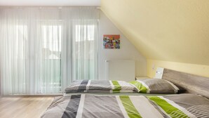 Een slaapkamer met twee bedden, dunne gordijnen, een radiator en een schilderij aan de muur.