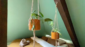 A bed with a brown blanket and pillows, two hanging planters with green plants, and a rope tied to the ceiling. - Urban hut (Sarreguemines)