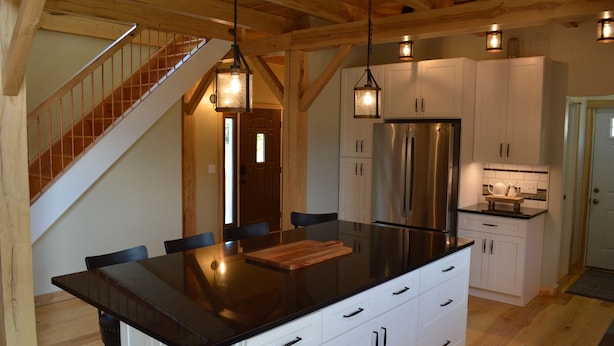 A modern kitchen with a central island, white cabinetry, stainless steel appliances, and a wooden staircase.