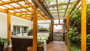 A covered patio area with a wooden pergola, a cushioned seating area, and potted plants. - Room 'Provence' with Shared Terrace and Wi-Fi (Birstein)