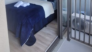 Un dormitorio con cama, un cuadro, aire acondicionado y un balcón con barandilla.