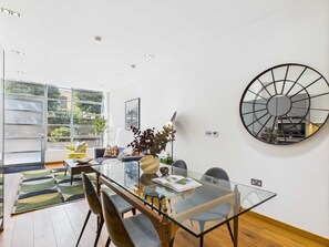 Un comedor moderno con una mesa de vidrio, sillas de madera y vistas al exterior a través de grandes ventanales.