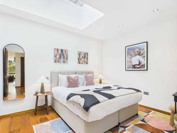 A modern bedroom with a large bed, a skylight, a mirror, and two abstract paintings.