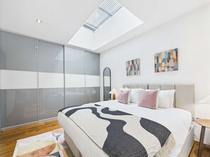 Un dormitorio moderno con tragaluz, una cama con ropa de cama estampada, un espejo grande y arte abstracto en la pared.