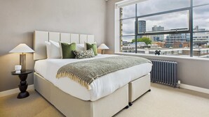 A modern bedroom with a large bed, a city view through a large window, and a hanging light fixture.