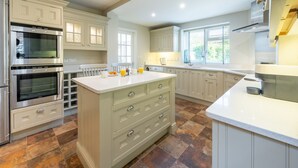 A spacious kitchen with white cabinetry, two built-in ovens, a large island with drawers, and a window providing natural light. - Creake Cottage, Burnham Market, Norfolk (Burnham market)