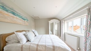 A bedroom with a large bed, a bedside table, a wardrobe, and a window with curtains. - Creake Cottage, Burnham Market, Norfolk (Burnham market)