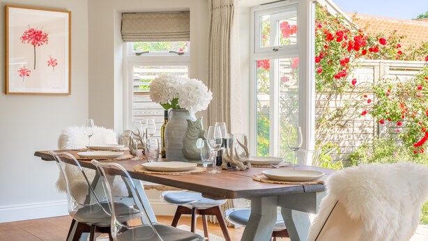 A dining area with a wooden table set for six, clear chairs, and a vase of white flowers. - Creake Cottage, Burnham Market, Norfolk (Burnham market)