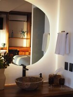 Un baño moderno con un espejo grande, un lavamanos de madera, un perchero para toallas y una pequeña planta.