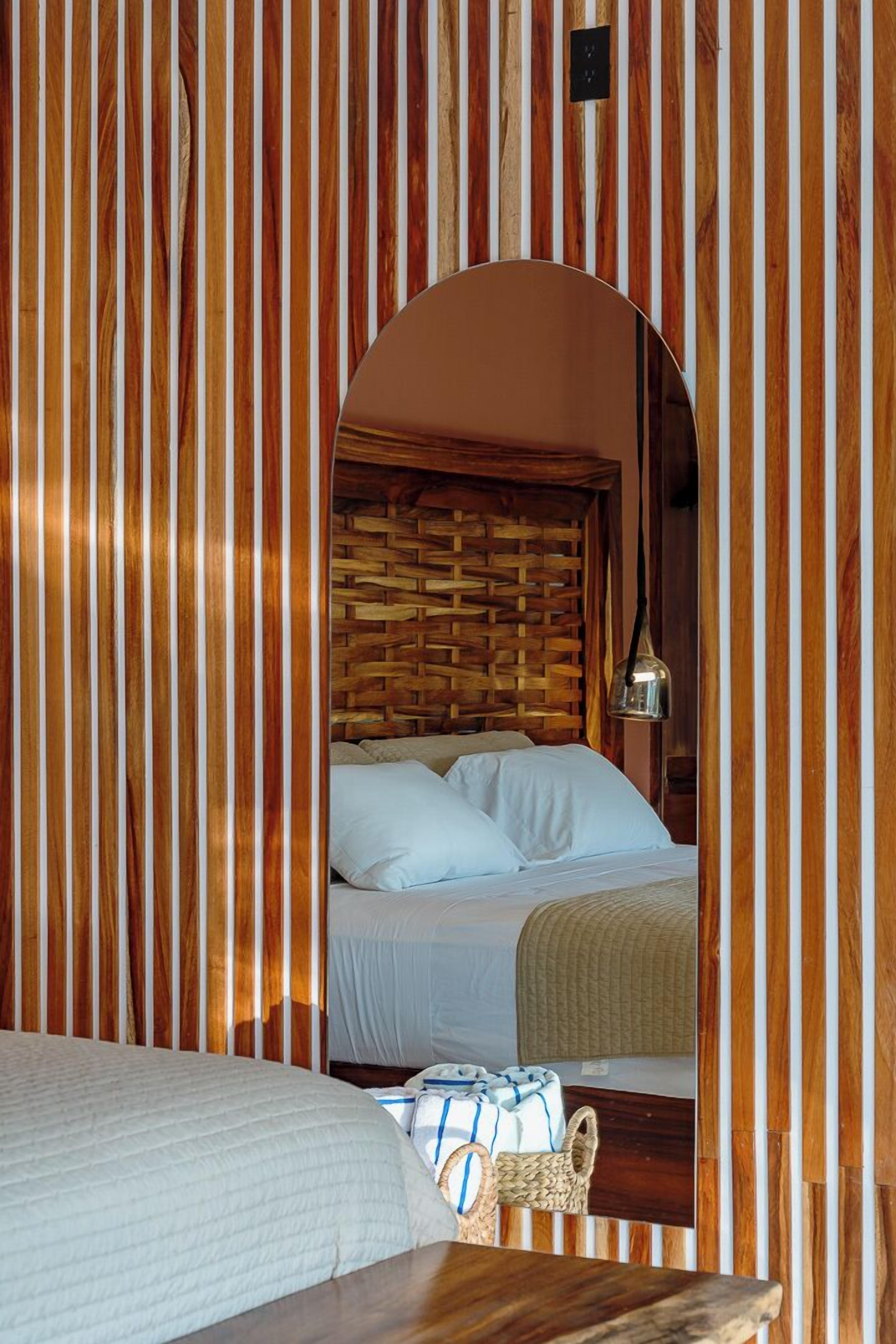 Una habitación con cama, cabecero de madera, pared tejida y lámpara colgante.
