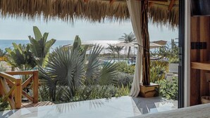 Ein Schlafzimmer mit einem großen Bett, Blick auf den Strand und einem mit Stroh gedeckten Dachstuhl.