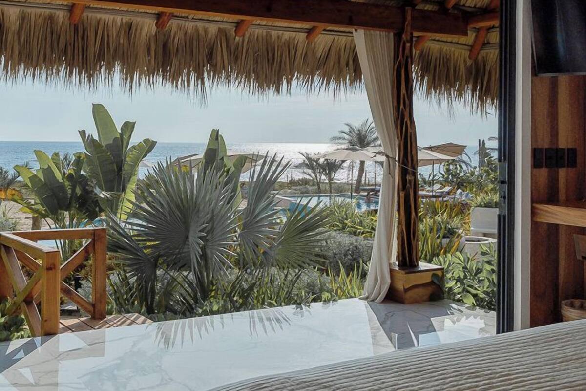 Un dormitorio con una cama grande, vista a la playa y una estructura de techo de paja.