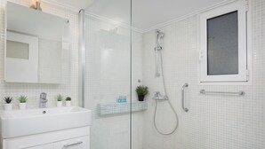 A modern bathroom with a glass shower enclosure, a white sink, and a small window.