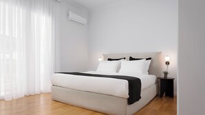 A modern bedroom with a large bed, white walls, and a wooden floor.