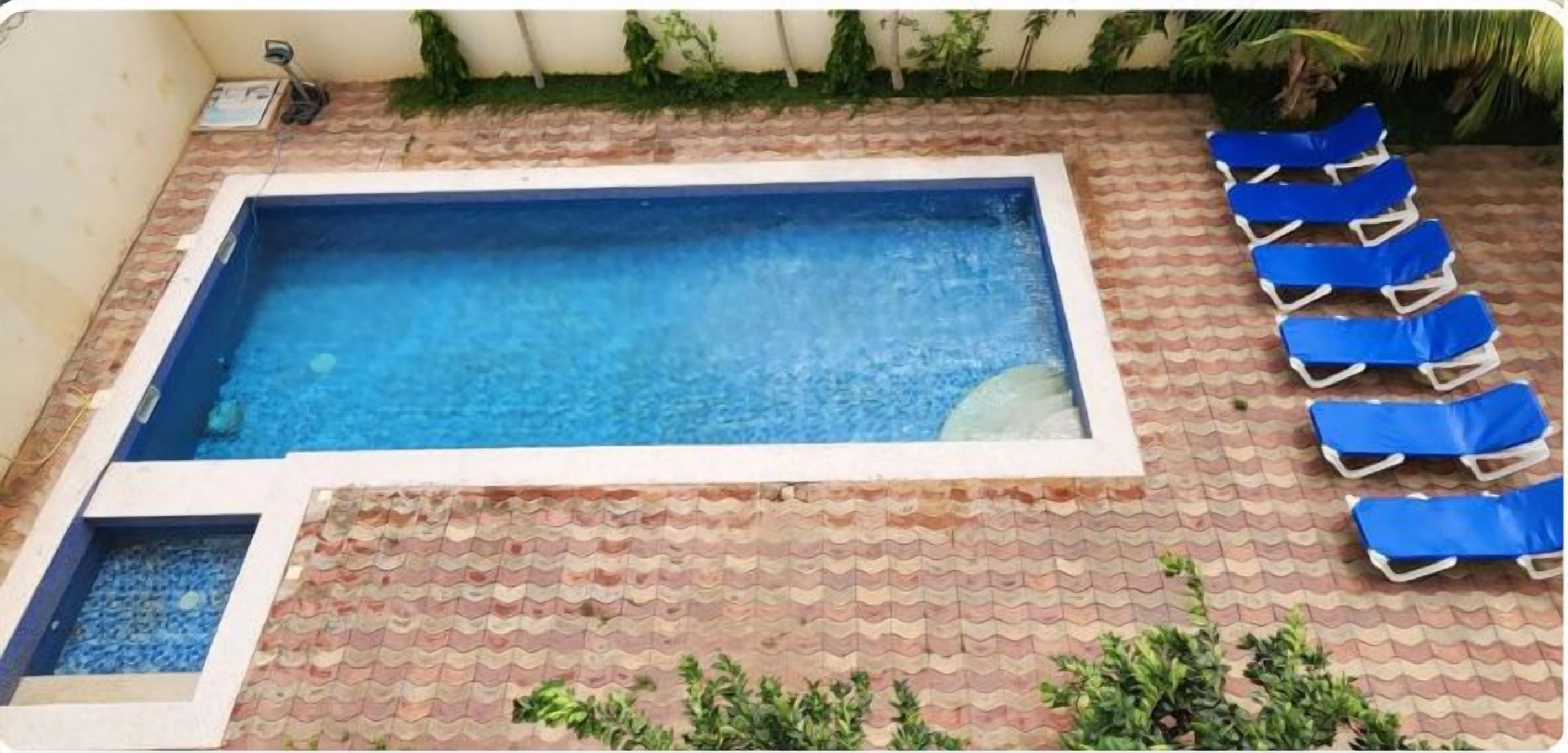 A rectangular swimming pool with a tiled deck, a small water feature, and blue lounge chairs arranged on one side.