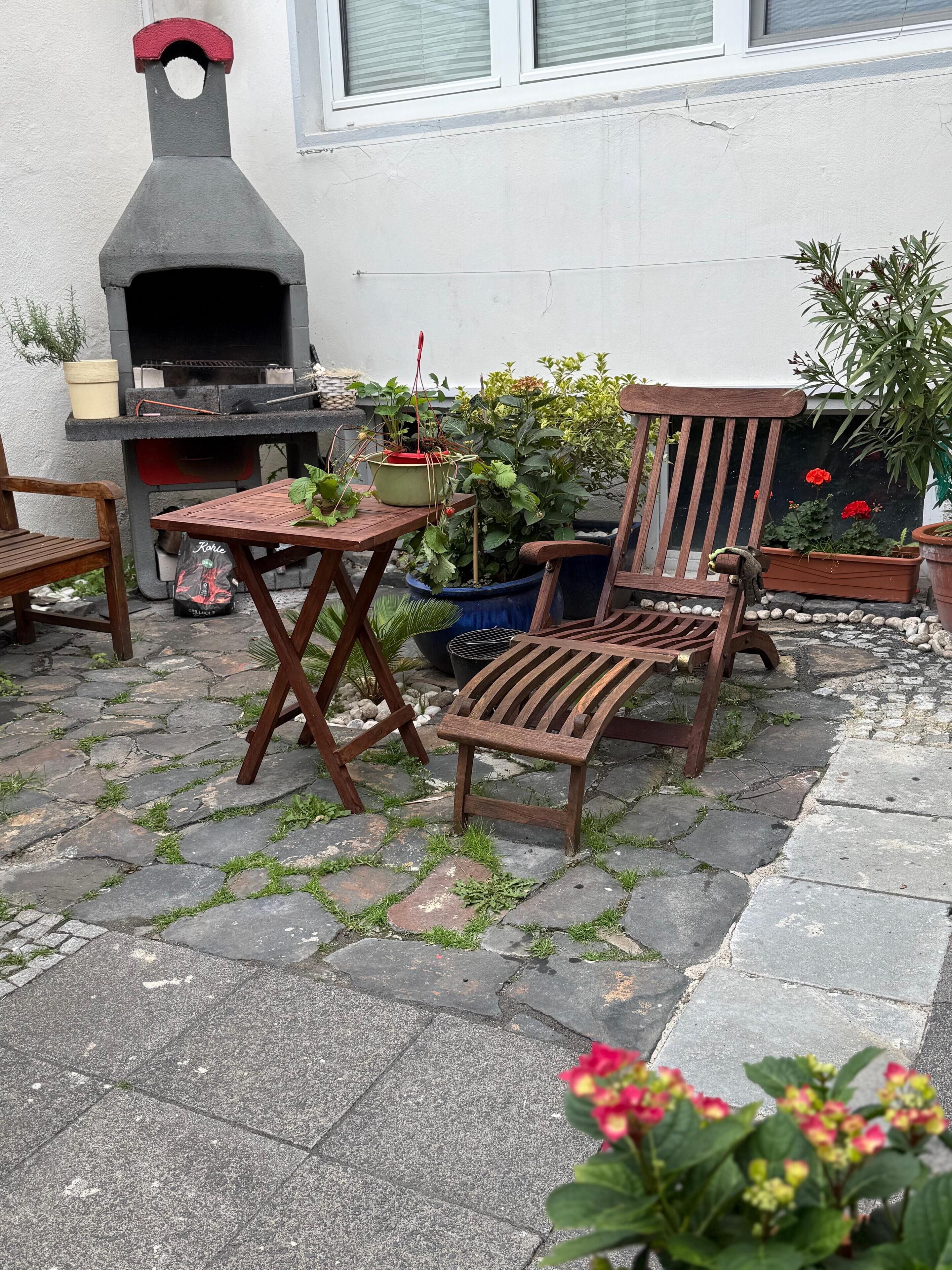Une terrasse extérieure avec un sol carrelé en pierre, une table en bois, une chaise en bois et un four à pizza.