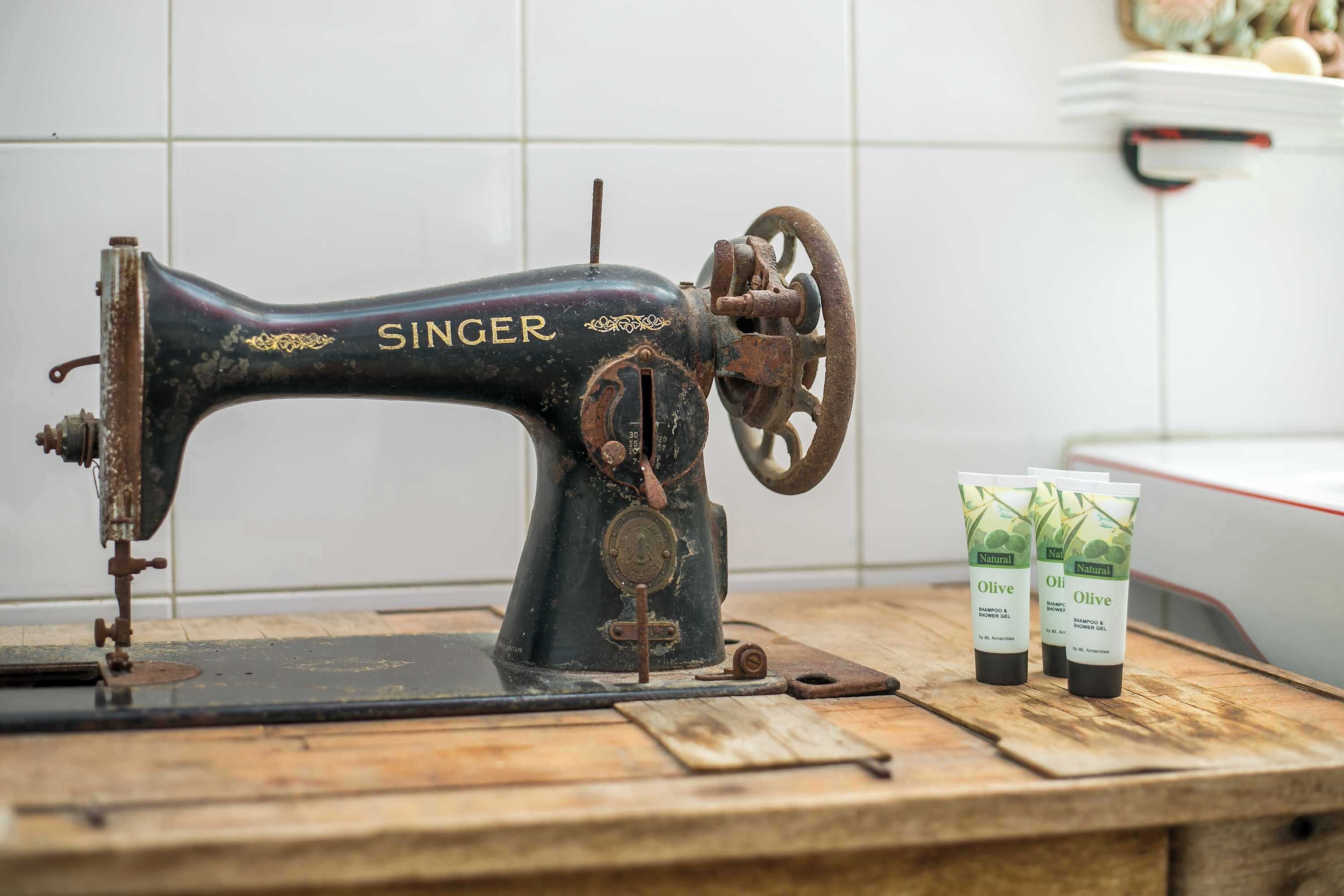 Eine alte Nähmaschine von Singer auf einem Holztisch, zusammen mit zwei Flaschen natürlichem Oliven-Shampoo.