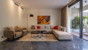 A modern living room with a sectional sofa, two armchairs, a coffee table, and a large window offering a view of greenery. - Kennah Catalina | West Golf Extension, New Cairo (New Cairo)