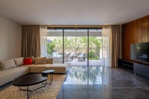 Una sala de estar moderna con un sofá, una mesa de centro y un televisor. Hay una puerta corrediza de vidrio que da a un área exterior con una hamaca y una terraza de madera.