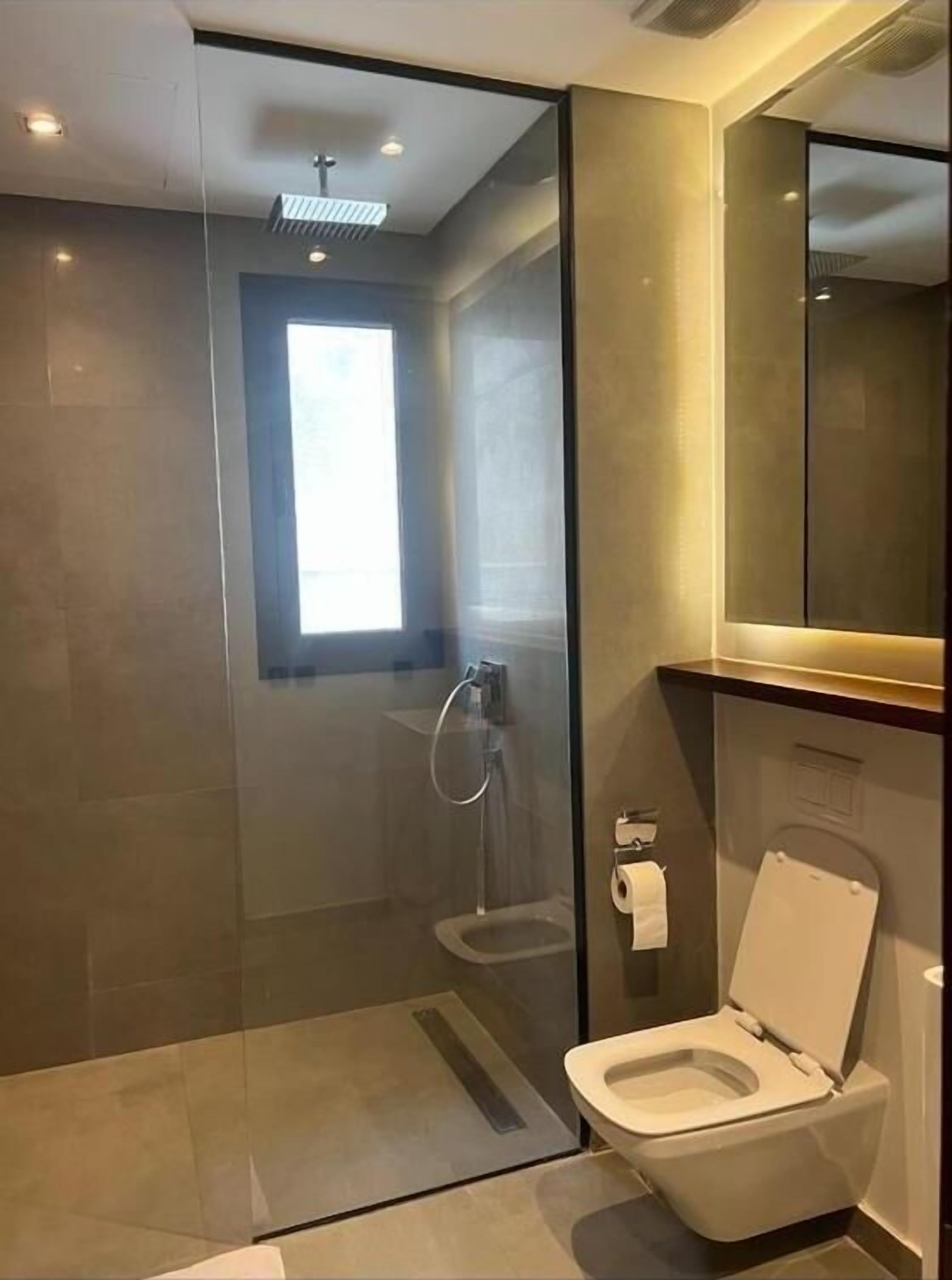 A modern bathroom with a glass-enclosed shower, a toilet, and a large mirror.