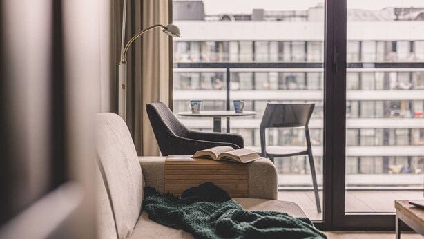 Una sala de estar acogedora con un sofá, una mesita y un sillón. Hay un libro sobre la mesa y una manta en el sofá.