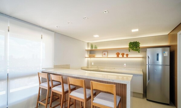 A modern kitchen with a central island, bar stools, a refrigerator, and a hanging plant. - Sea View Studio in Condominium With Pool Edf1707 (Salvador)