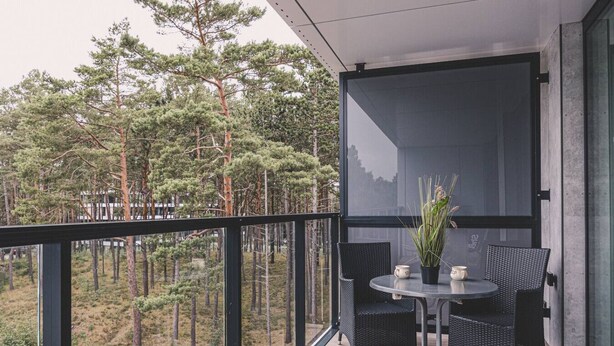 A balcony with a table and chairs, overlooking a forested area. - Puro - Modern Apartment by the Dunes (Trzebiatow)