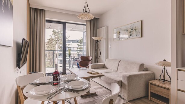 Una sala de estar moderna con sofá, mesa de comedor y sillas. Hay una ventana con cortinas, una lámpara de pie y un cuadro en la pared.