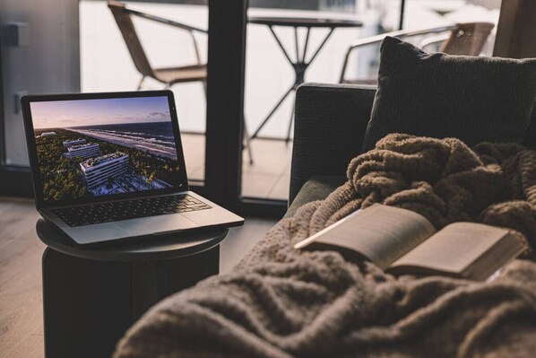 A laptop on a small table with a book and a blanket.