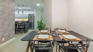 A modern dining area with a black table set for four, surrounded by black chairs. A plant is visible in the background, and the room has a minimalist design with white walls and a gray floor. - Apart in Cond. w/ Pool 400m From the Beach Tdb0101 (Florianópolis)