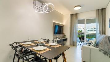 A modern dining area with a table set for four, a flat-screen TV mounted on the wall, and a balcony with a view of the city.