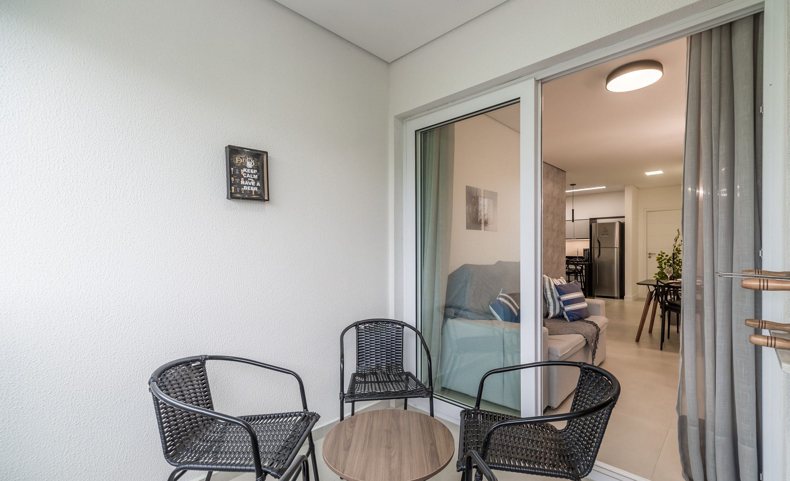 A balcony with wicker chairs and a round table, a sliding glass door leading to a living area with a sofa and a coffee table.