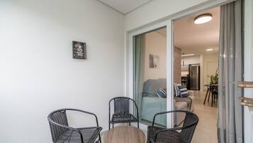 A balcony with wicker chairs and a round table, a sliding glass door leading to a living area with a sofa and a coffee table.