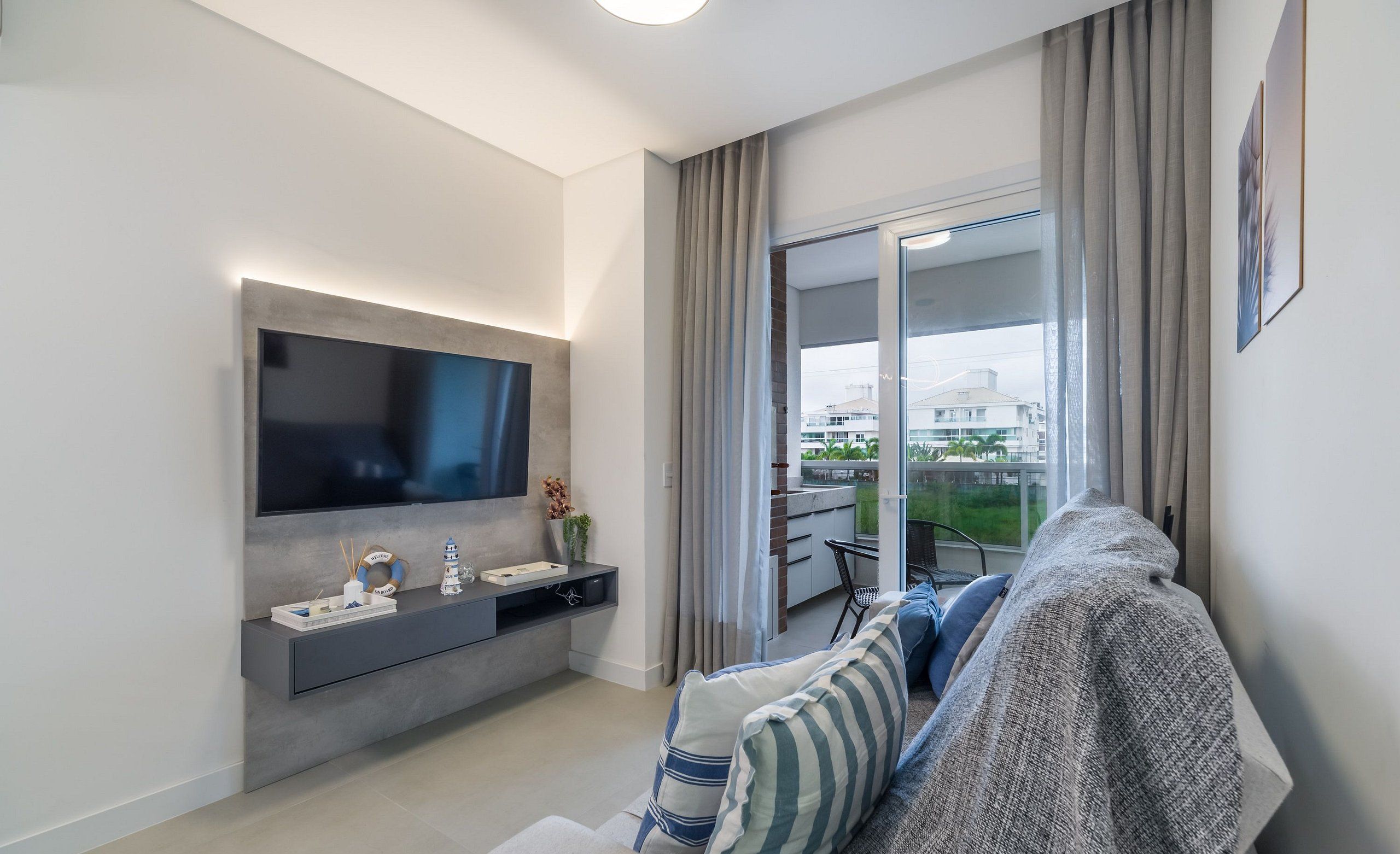 Una sala de estar moderna con televisor de pantalla plana, sofá gris y puerta corrediza de vidrio que da a un balcón.