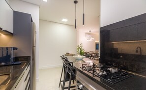 Une cuisine moderne avec un plan de travail noir, des appareils en acier inoxydable et des luminaires suspendus.