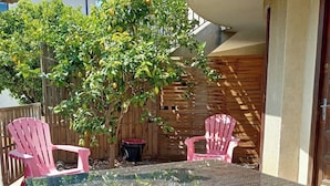 Une table à plateau en verre, des chaises en osier, une clôture en bois et un arbre aux feuilles vertes.